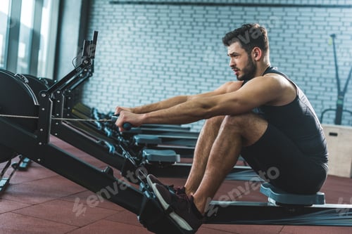 Preview: Side view of sportsman doing exercise on rowing machine in sports center