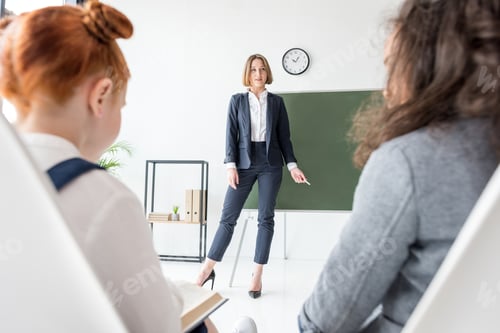 Preview: smiling young teacher holding chalk and looking at schoolkids during lesson