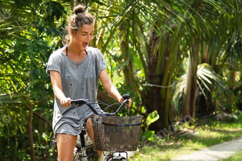 Preview: Happy woman riding bicycle in the tropical garden at hot summer day