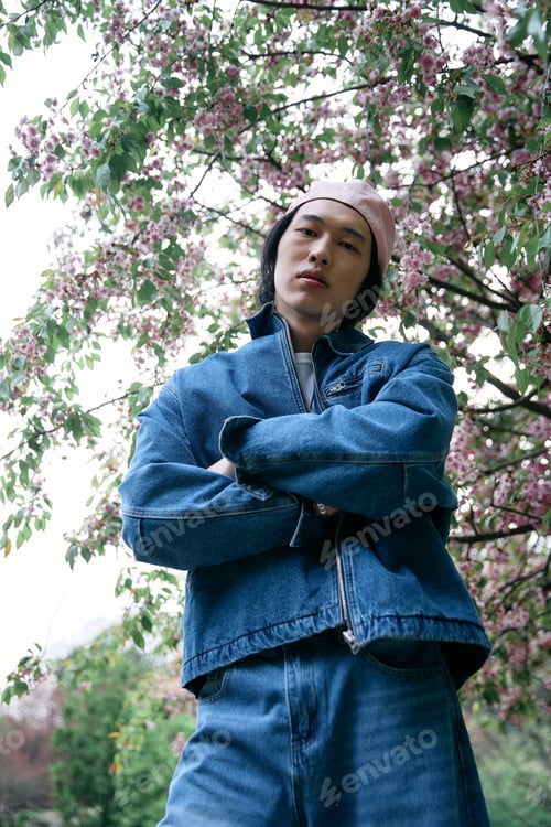 Preview: Young man showcases stylish denim look amidst blooming park scenery