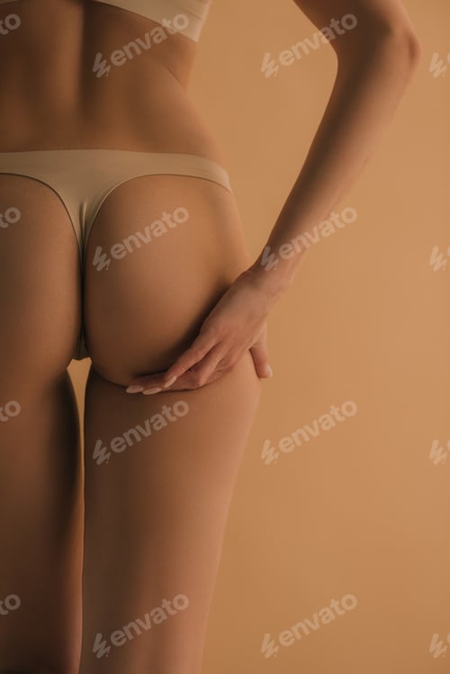 Preview: Back view of young woman in panties touching butt isolated on beige, cropped view
