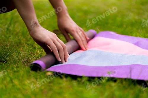 Preview: a woman rolls a sport mat before a yoga class outdoors on the grass