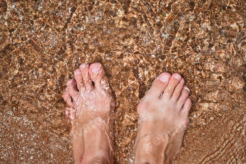Preview: Close up of barefoot legs in the water, top view