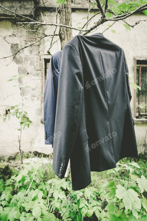 Preview: Vertical shot of some coats hanging from the branches of a tree in the yard by an old house