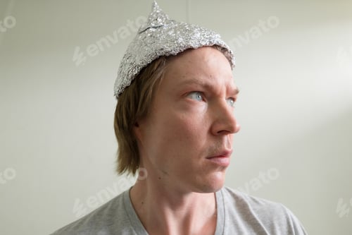 Preview: Face of young man with tin foil hat thinking inside the room