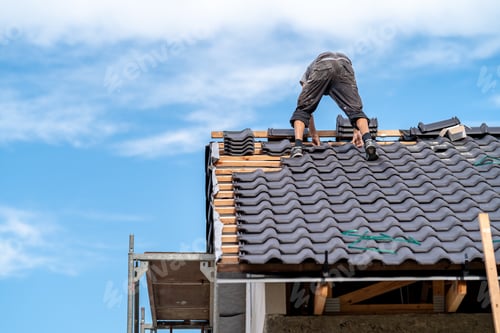 Preview: ceramic roof of a new building, worker installs tiles on wooden beams