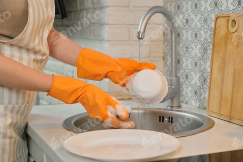 Preview: Young woman in apron gloves washing dishes with sponge and detergent