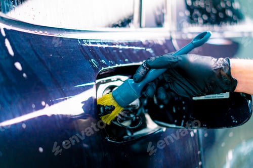 Preview: Close-up of a car wash employee washing the fuel cap space of a luxury blue car using a brush