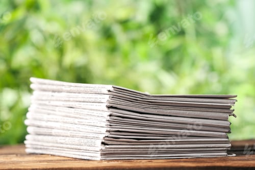 Preview: Stack of newspapers on wooden table against blurred green background. Journalist's work