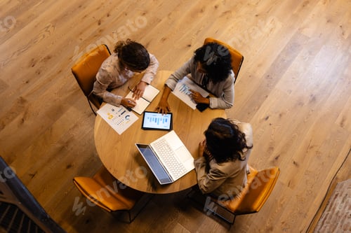 Preview: Diverse female colleagues in discussion using laptop and tablet in casual office meeting