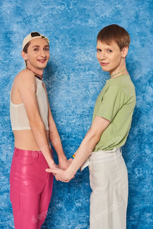 Preview: Smiling homosexual friends holding hands and looking at camera during gay pride month celebration on