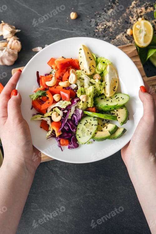 Preview: Fresh vegetable salad in female hands against the background of a dark tabletop.