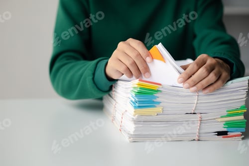 Preview: A person sits in an office with a huge stack of papers, she is a company employee, managing paperwor