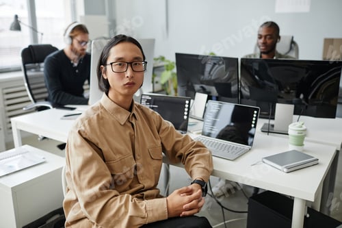 Preview: Serious Asian businessman in eyeglasses and casual clothes sitting by workplace