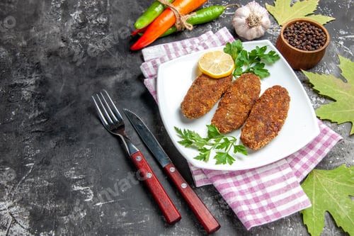 Preview: bottom view cutlets lemon slice parsley on white plate fork and knife black and red pepper garlic