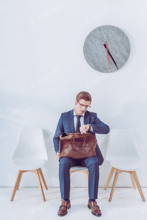 Preview: handsome employee in glasses holding briefcase and looking at watch