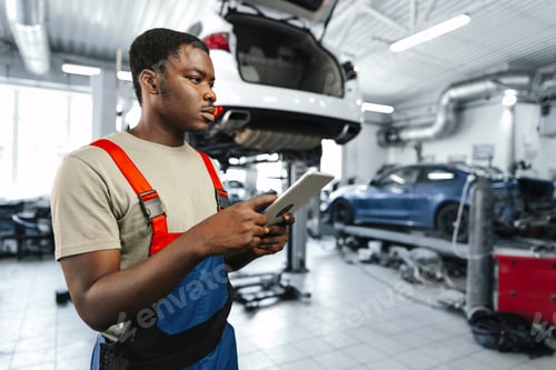 Preview: Young African auto mechanic using digital tablet in a car service