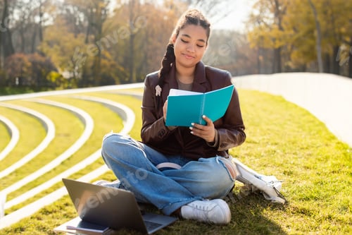 Preview: Young Woman Reads Book in Park, with Laptop