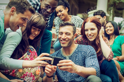Preview: A group of friends on the steps of a house porch, looking at a smart phone selfy on the screen.