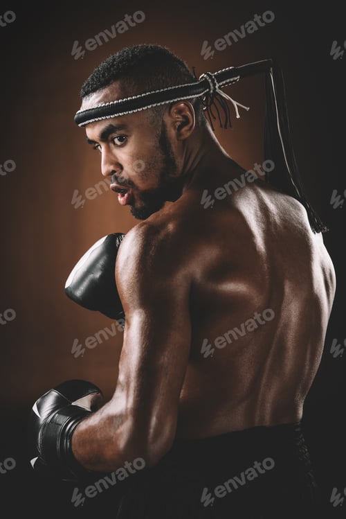Preview: Young shirtless Muay Thai fighter with boxing gloves looking over shoulder, action sport concept