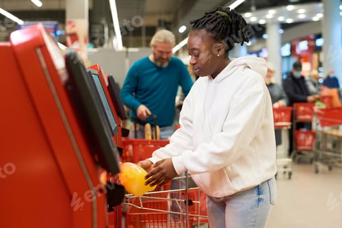Preview: Young female consumer scanning bottle of juice while using self service terminal