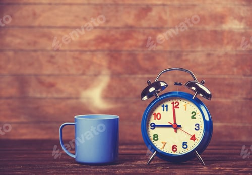 Preview: Cup of coffee and alarm clock on wooden table.