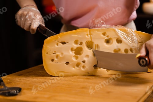 Preview: Cheese sommelier slicing aged Maasdam with knife in shop