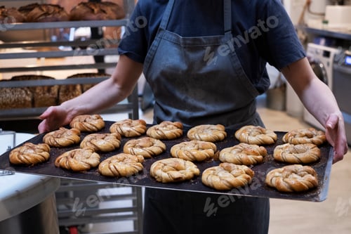 Preview: Close up of person holding tray with freshly baked cinnamon buns in an artisan bakery.