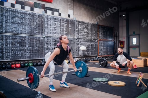 Preview: Young man watching woman lift barbell in gym