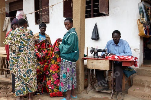 Preview: Tailor at work with vibrant textiles as customers look on
