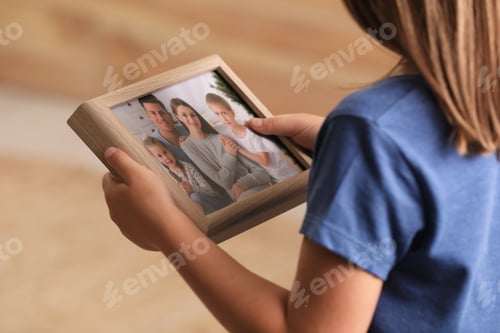 Preview: Little girl holding framed family photo on blurred background, closeup