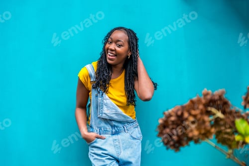 Preview: Casual african woman posing shy leaning on a blue wall