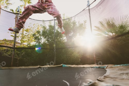 Preview: Little girl enjoying her vacation jumping on the trampoline doing acrobatic exercise outdoors.
