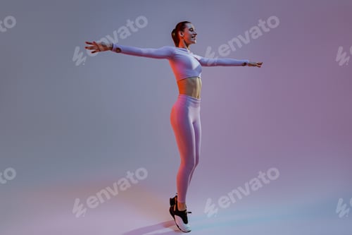Preview: Happy sporty woman wearing sportswear stand with raised up arms on studio background