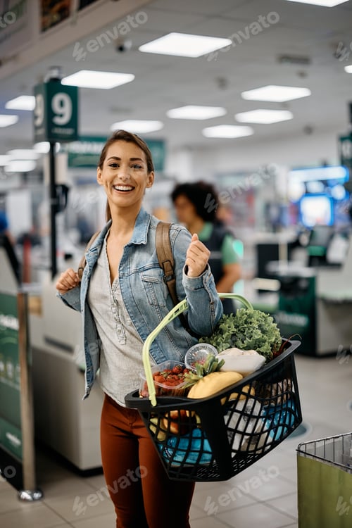 Preview: Happy woman with full shopping basket in supermarket looking at camera.