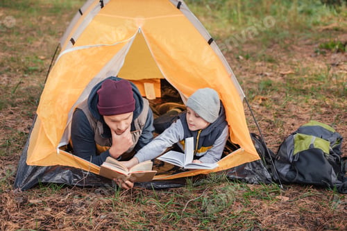 Preview: father and son reading books while lying in tent in autumn forest