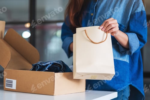 Preview: a woman opening a shopping bag with postal parcel box of clothing for delivery and online shopping