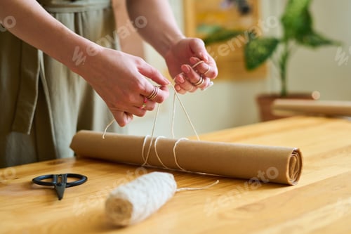 Preview: Hands of young female clerk or artisan tying white thread over roll of paper