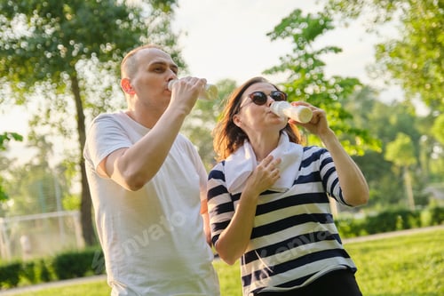 Preview: Happy mature couple in park, resting drinking yogurt, dairy after sports exercises