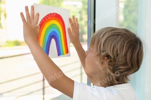 Preview: Little boy holding rainbow painting near window indoors. Stay at home concept