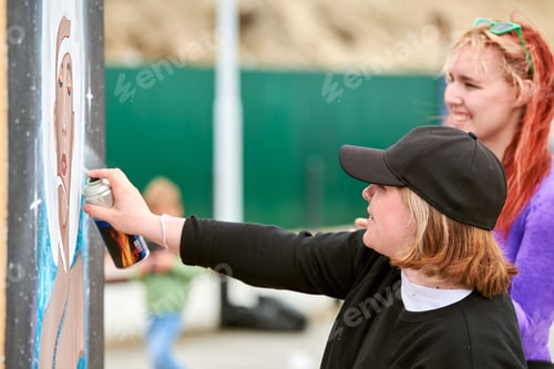 Preview: Two female artists painting picture with paint spray can spraying onto canvas at street exhibition