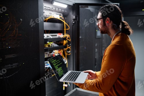 Preview: Bearded IT engineer using laptop while setting up network in server room