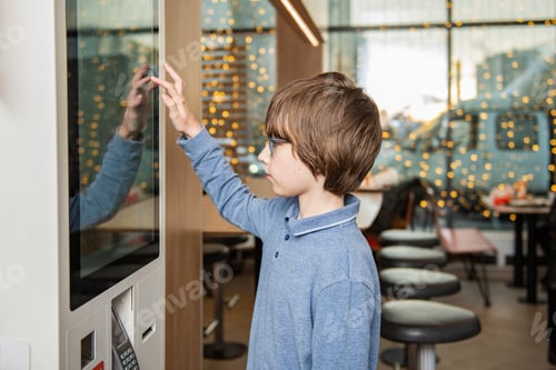 Preview: A boy using a touchscreen kiosk to place an order in a modern cafe interior with warm bokeh lights.