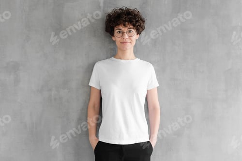 Preview: Attractive young woman posing in blank white cotton t-shirt, standing against gray wall
