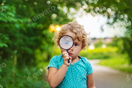 Preview: A child looks through a magnifying glass in nature. Selective focus.
