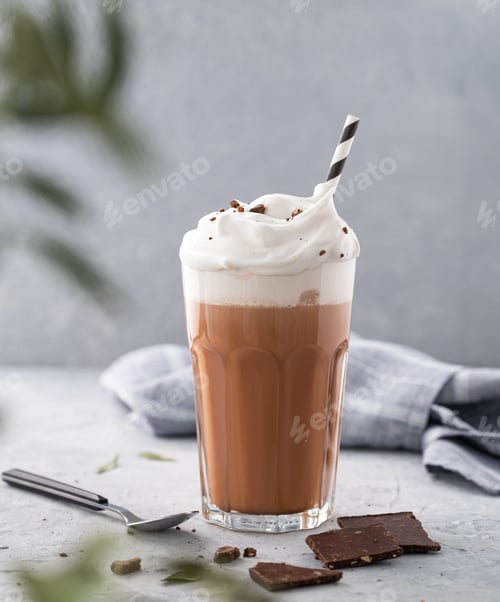 Preview: Hot chocolate with whipped cream and chocolate pieces in a glass on a blue background with a branch
