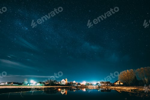 Preview: Belarus, Eastern Europe. Night Sky Stars Above Countryside Landscape With Lake Coast And Small Town