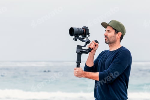 Preview: male on the beach holding a camera on a gimbal or stabilizer filming