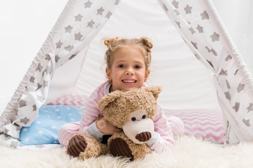 Preview: adorable little kid with teddy bear lying on floor in handcrafted teepee