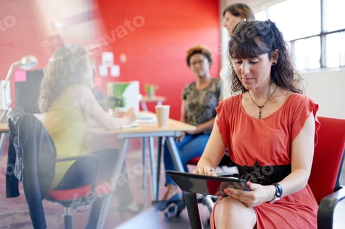 Preview: Confident female designer working on a digital tablet in red creative office space